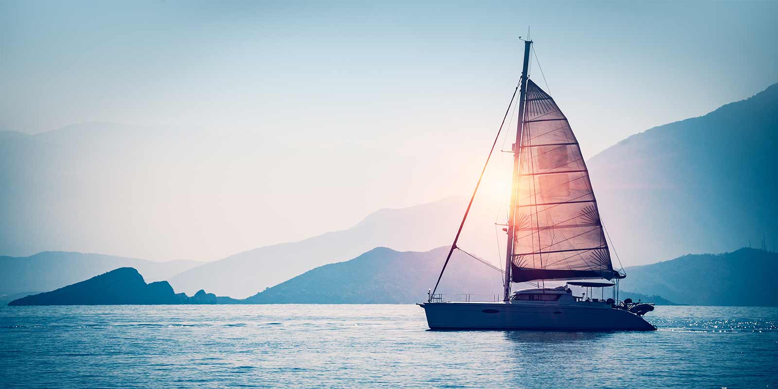 a sailboat out at sea during a sun set with mountains in the back