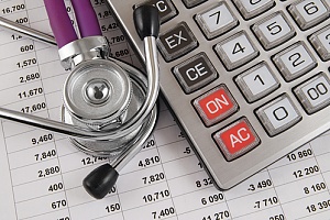 a stethoscope with a calculator and medical expenses spreadsheet on a desk