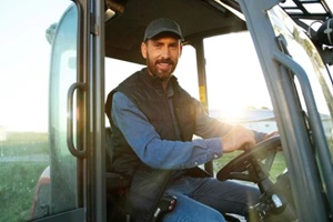 portrait of young caucasian male farmer in cap sitting in tractor with open door and smiling to camera