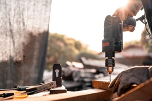 carpenter using a drilling tool or an electric screwdriver is working at home on the wooden floor