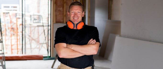 attractive and confident constructor carpenter or builder man with ear protection gear working happy at industrial construction site
