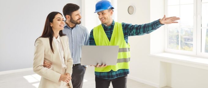 professional builder collaborates with a positive husband and wife to discuss a home renovation project using a laptop and blueprint