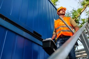 construction worker wearing safety vest and helmet climbing metal stairs with toolbox and level