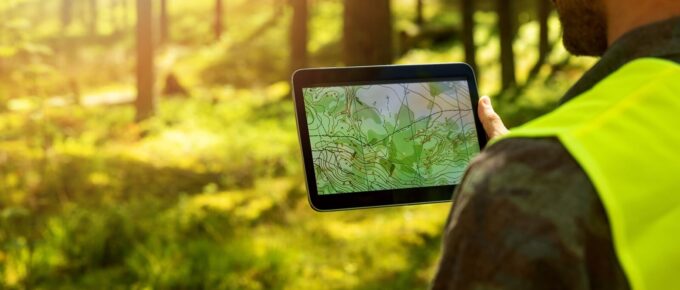 man working with topographic map data on digital tablet in forest