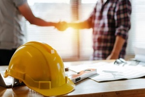 yellow safety helmet on workplace desk with construction worker team hands shaking greeting start up plan new project contract in office center 