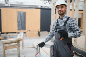 portrait of worker in uniform near prefabricated wooden house