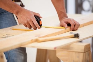 closeup of a contractor using a tape measure to cut some wood