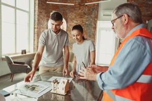 foreman or achitect engineer shows future house, office or store design plans and model to a young couple