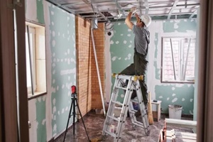 young builder makes a plasterboard ceiling, standing on a stepladder