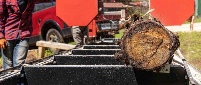 close up selective focus shot of a blurry man at work using an industrial portable sawmill to chop a tree trunk into logs - forestry insurance