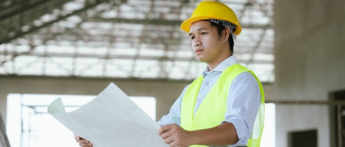 engineer in safety gear reviewing blueprints at a construction site