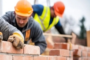 focused construction three bricklayers in orange hard hats and work gloves build a brick wall