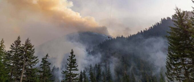 helicopter fighting wildfire over smoky forested mountains