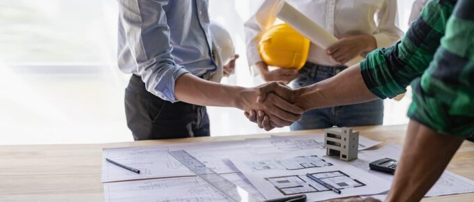 yellow hard hat on table and house design print design with construction team handshake greeting start new project contract plan